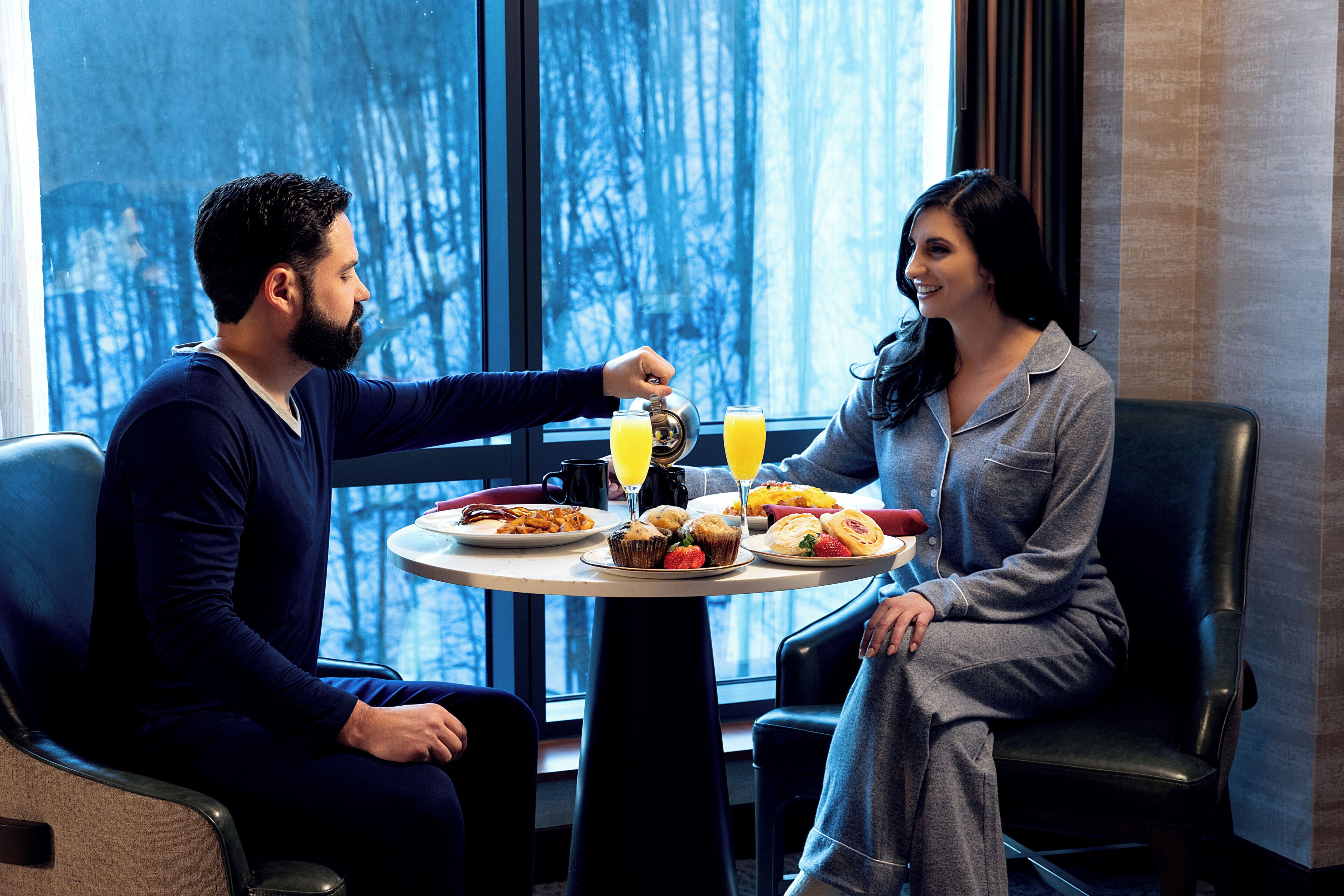 A couple seated at a table with breakfast, a window view, and a modern interior.