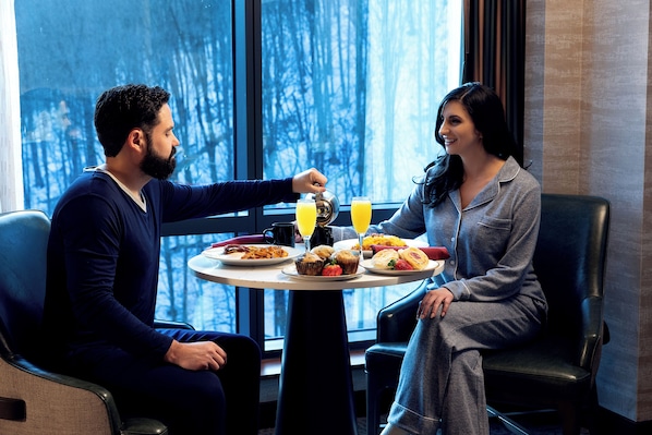 A couple seated at a table with breakfast, a window view, and a modern interior.