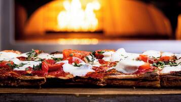 En pizza med tomater, basilika och mozzarella, serverad på en träbricka.