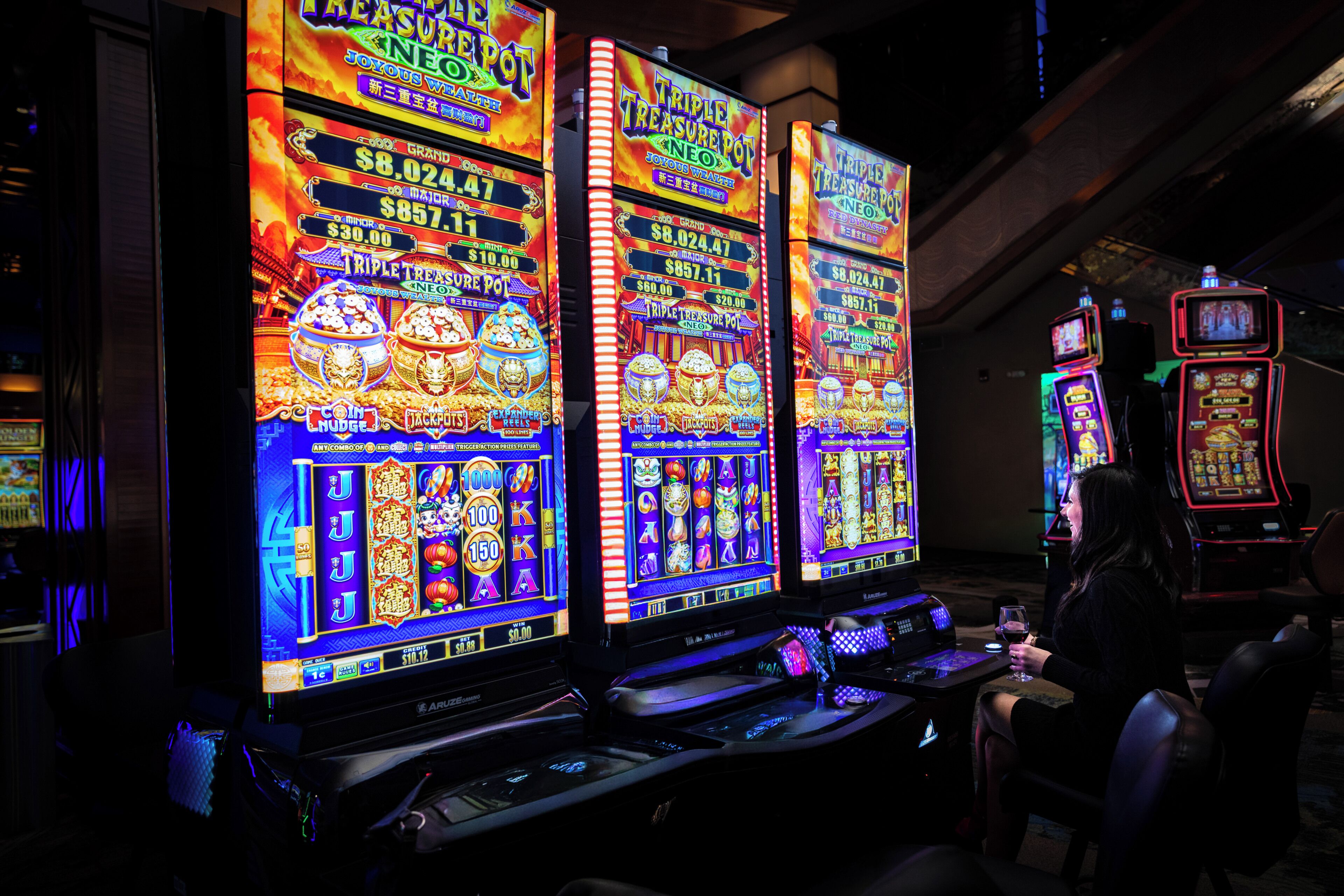 Slot machines in a dimly lit room with a woman seated at one.