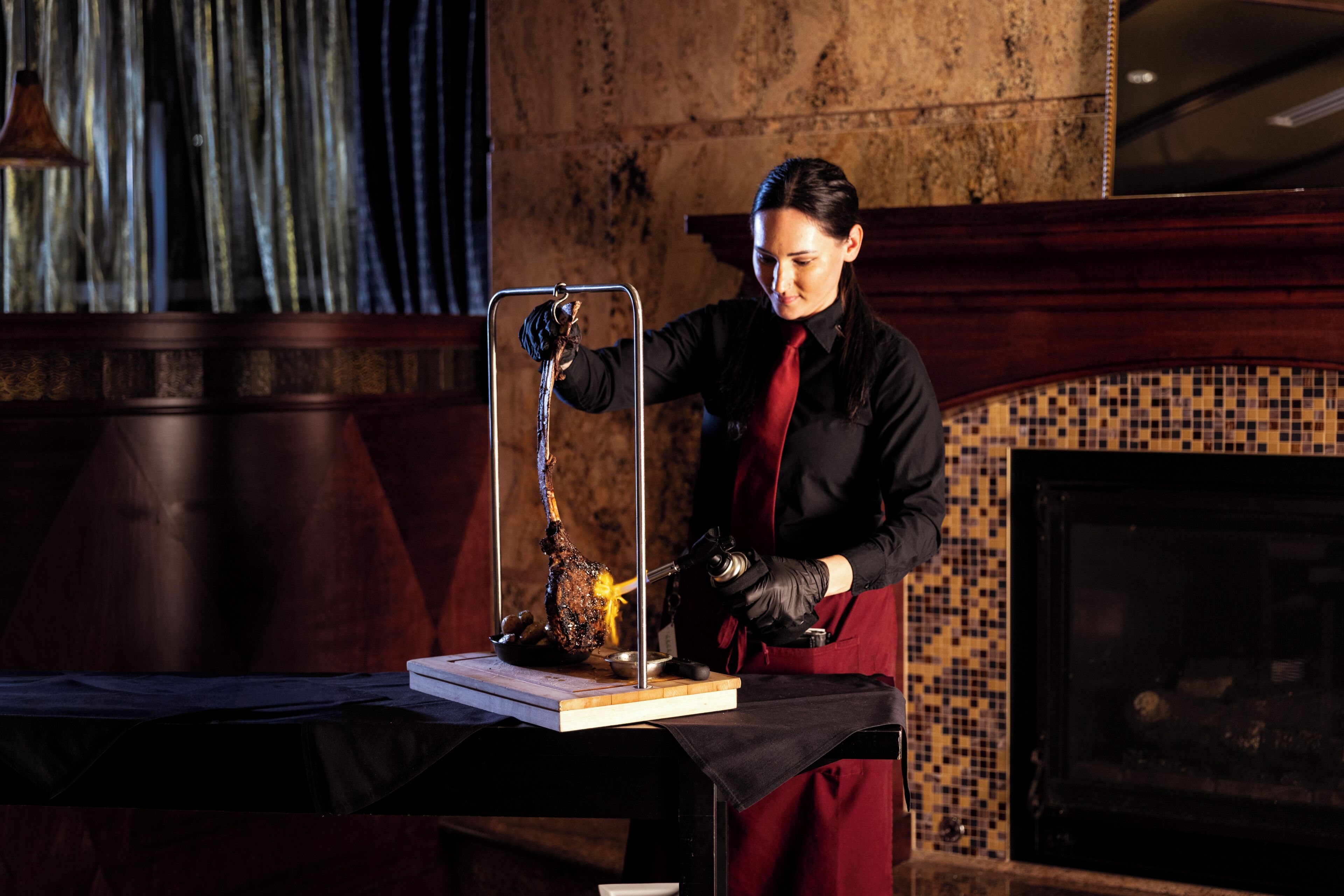 A person carving a large piece of meat on a wooden board, with a metal stand holding the meat.