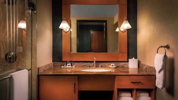 A bathroom with a marble countertop, a sink, a mirror, and two wall-mounted lights.
