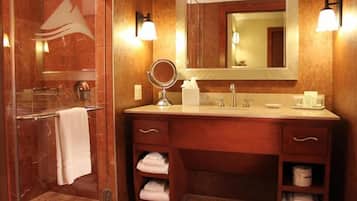 Une salle de bain avec une douche à parois de verre, un meuble-lavabo avec un miroir et un évier. Des serviettes et des articles de toilette sont posés sur le comptoir.