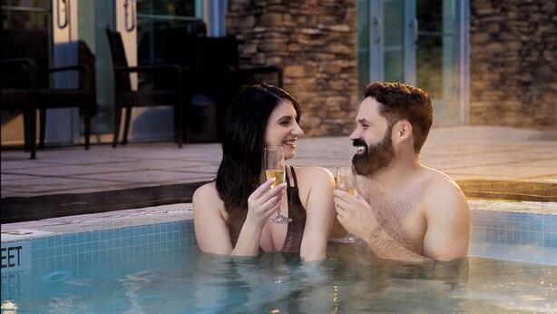 A couple in a hot tub with a stone wall and chairs in the background. - Seneca Allegany Resort & Casino (Salamanca)