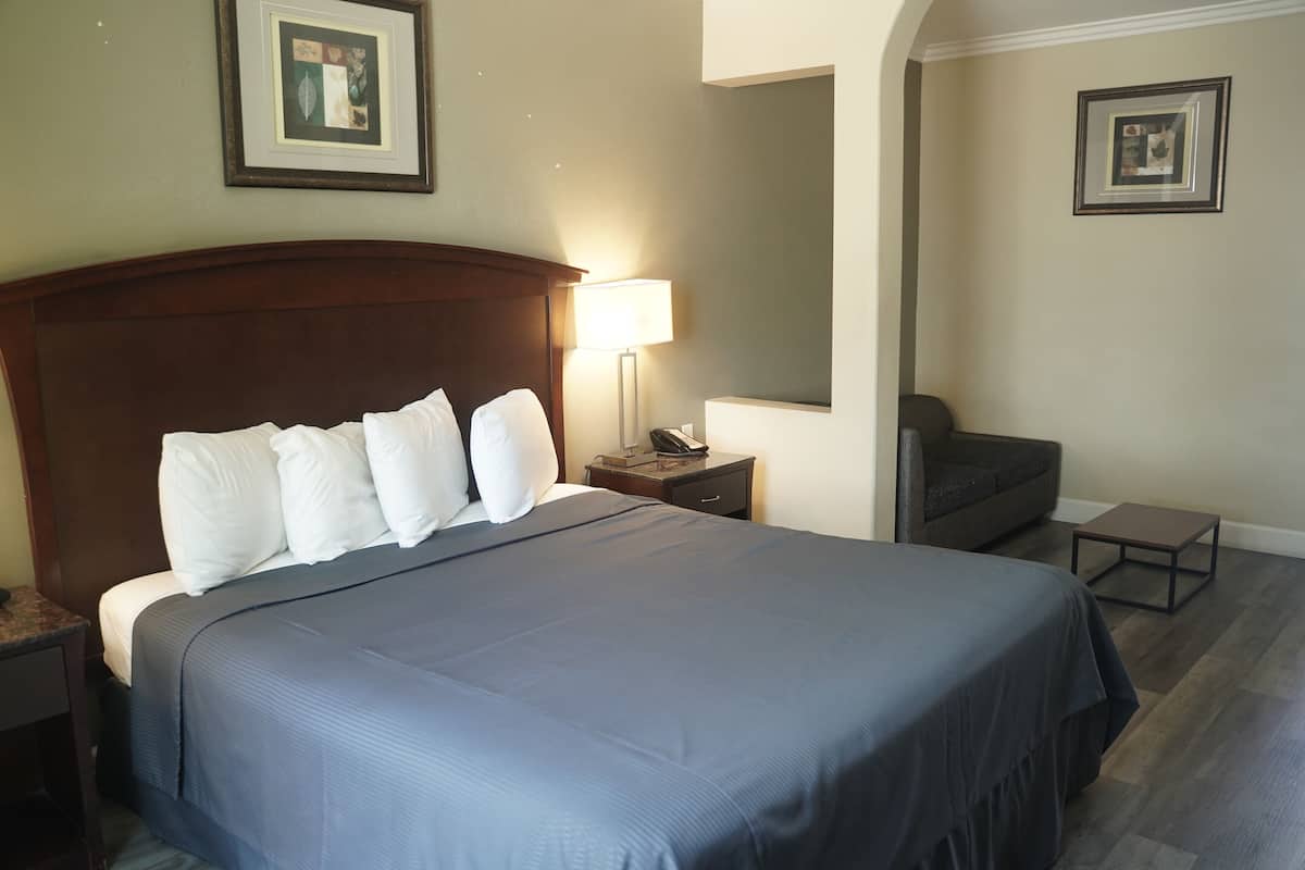 A neatly made bed with a dark blue bedspread and white pillows, a bedside lamp, a small table, and a dark-colored armchair.