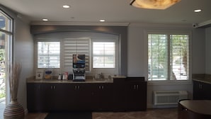A kitchen with dark cabinets, a built-in coffee maker, a trash bin, and a window with blinds. - Harbor Inn & Suites (Garden Grove)