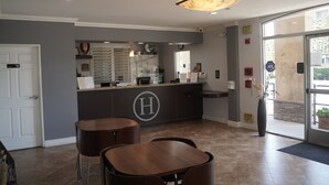 A reception area with a counter, two bar stools, a large H logo, and a glass door leading outside. - Harbor Inn & Suites (Garden Grove)