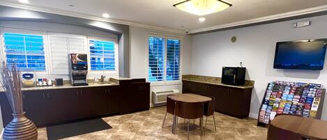 Una cocina moderna con muebles oscuros, una isla central, un televisor de pantalla plana montado en la pared y una ventana con persianas.