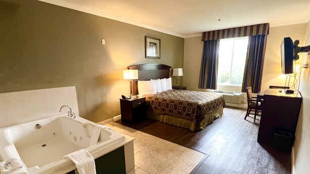 A hotel room with a large bed, a separate bathroom with a bathtub, a desk, and a chair. - Harbor Inn & Suites (Garden Grove)