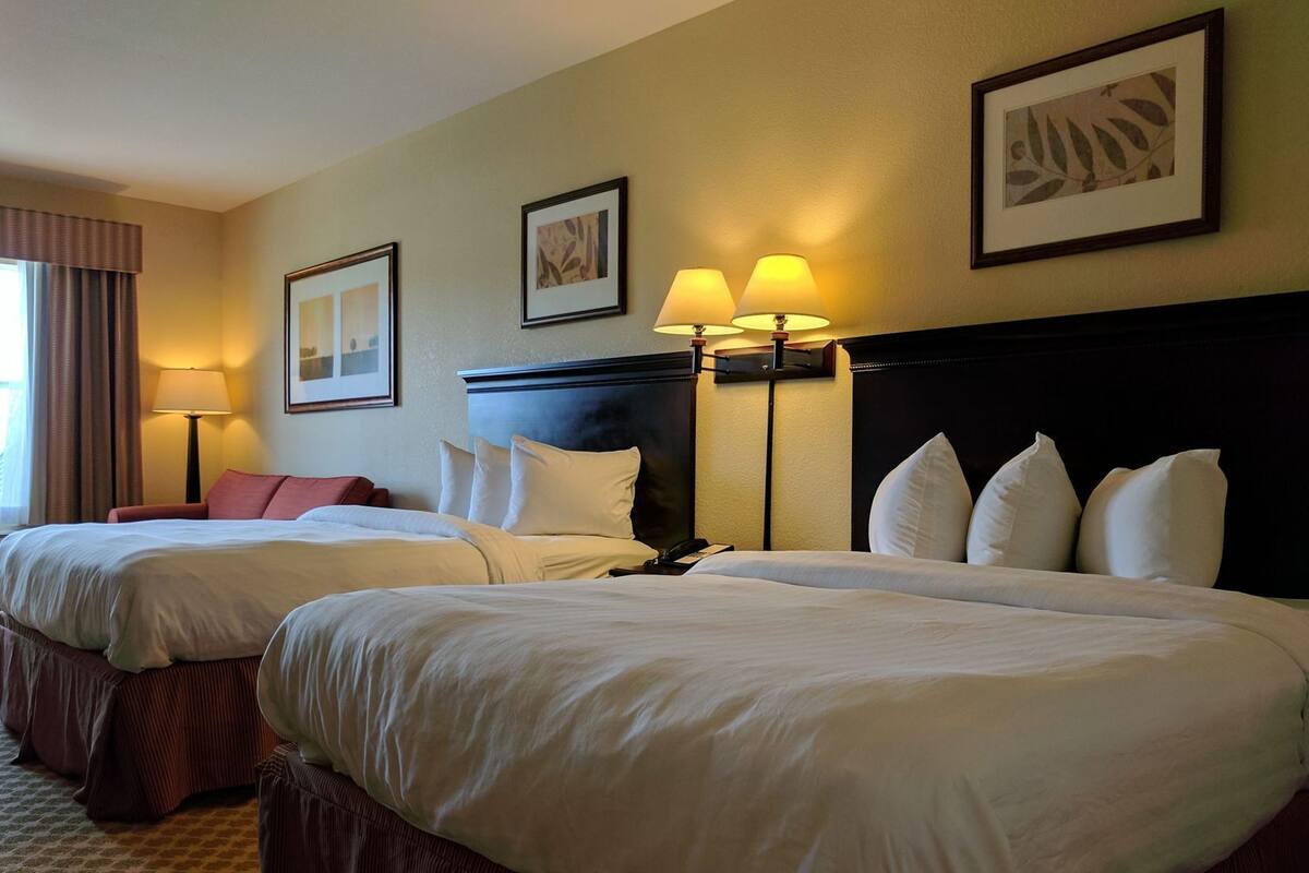 Habitación de hotel con dos camas, una mesita de noche, una lámpara y cuadros en la pared.