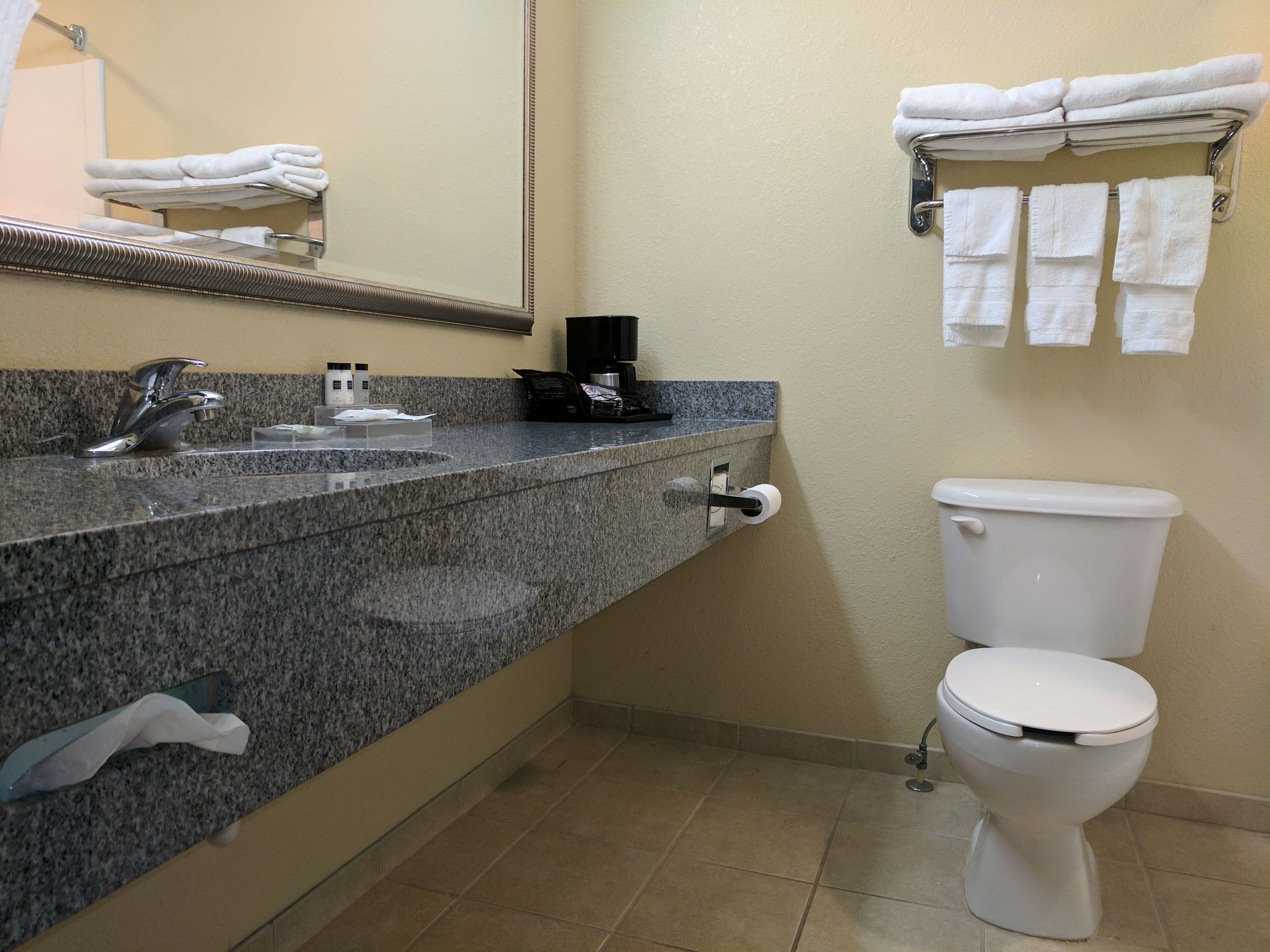 Un baño con encimera de granito, lavamanos, espejo, inodoro y toallero con toallas dobladas.