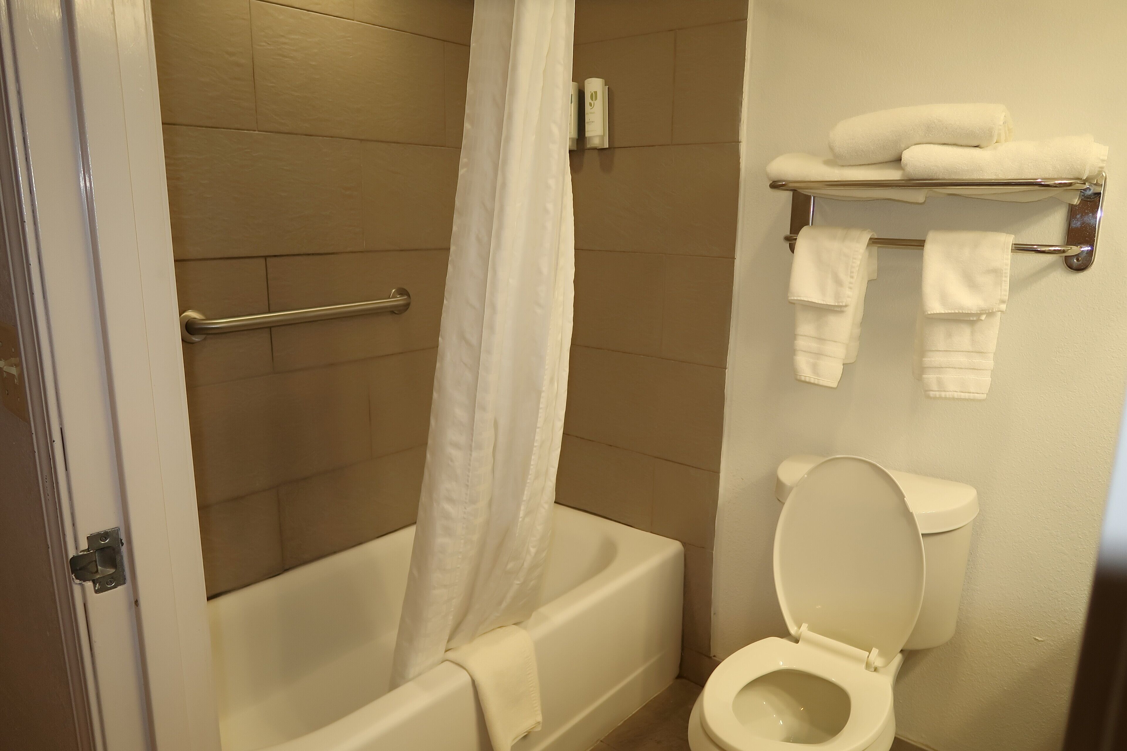 A bathroom with a bathtub, a shower curtain, a toilet, and a towel rack with towels.