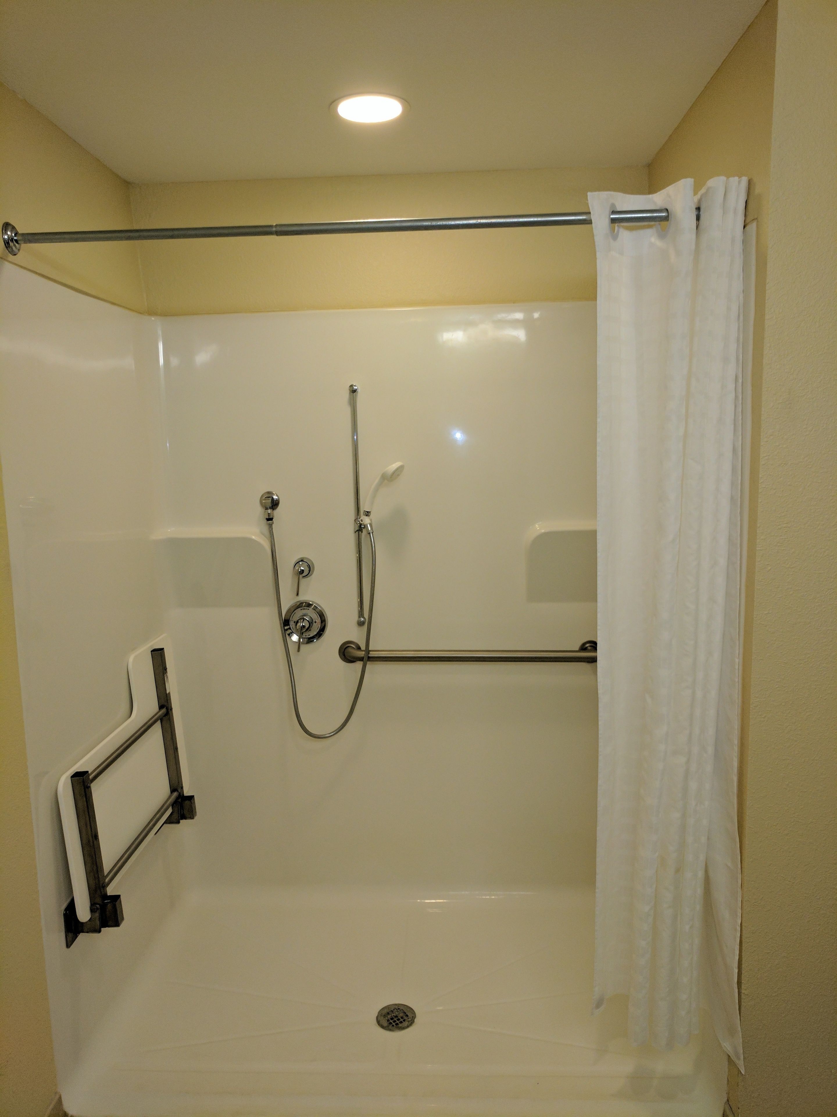 A walk-in shower with a grab bar, a showerhead, and a curtain.