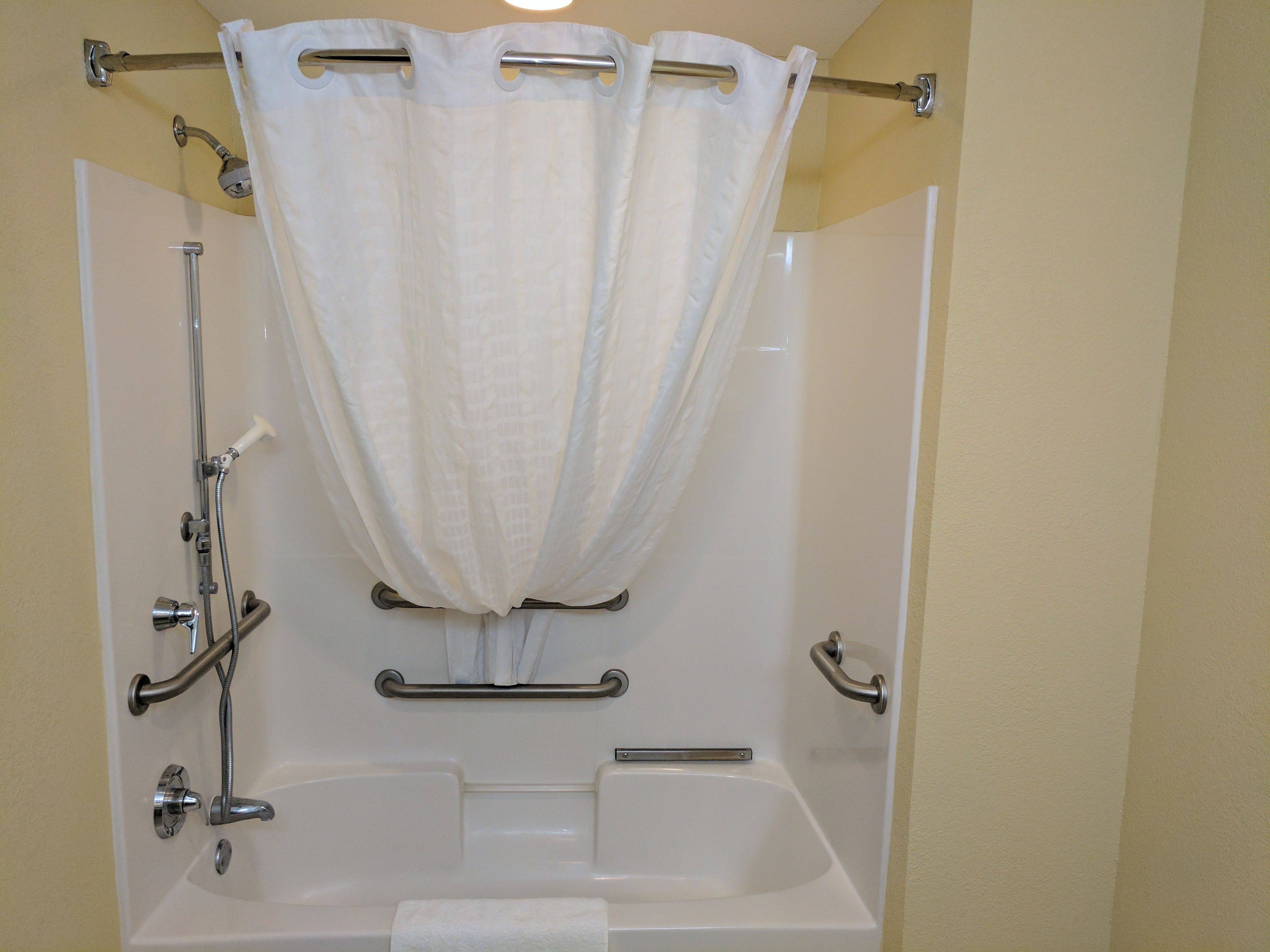A walk-in shower with a bathtub, grab bars, and a shower curtain.