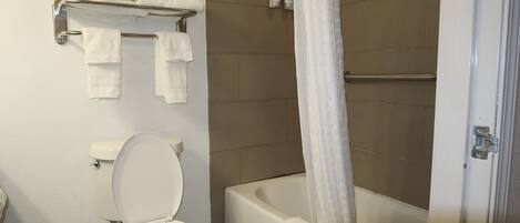 Une salle de bain comprenant des toilettes, une baignoire avec un rideau de douche et un porte-serviettes avec plusieurs serviettes.