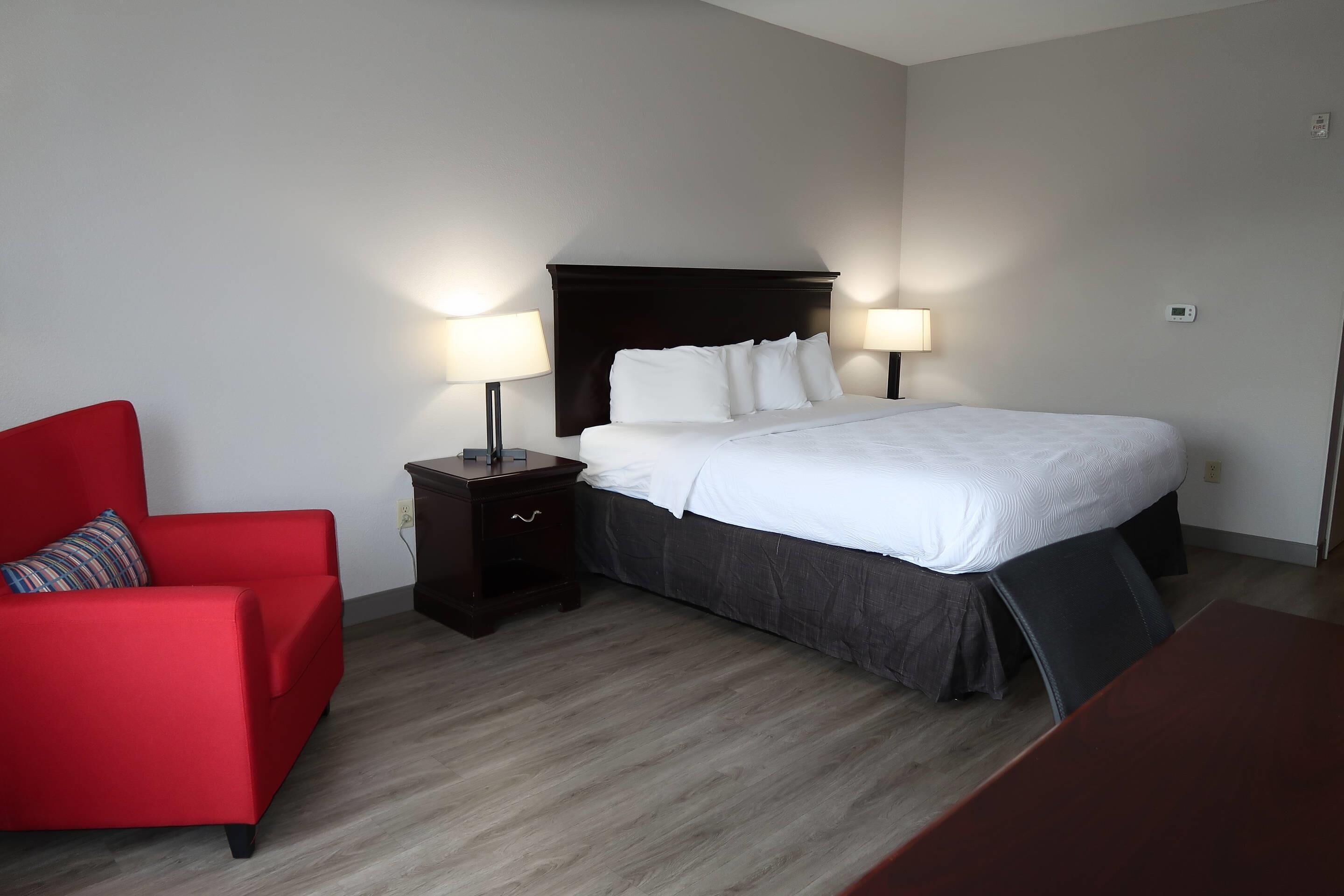 A hotel room with a bed, a nightstand, a red armchair, and a wooden table.