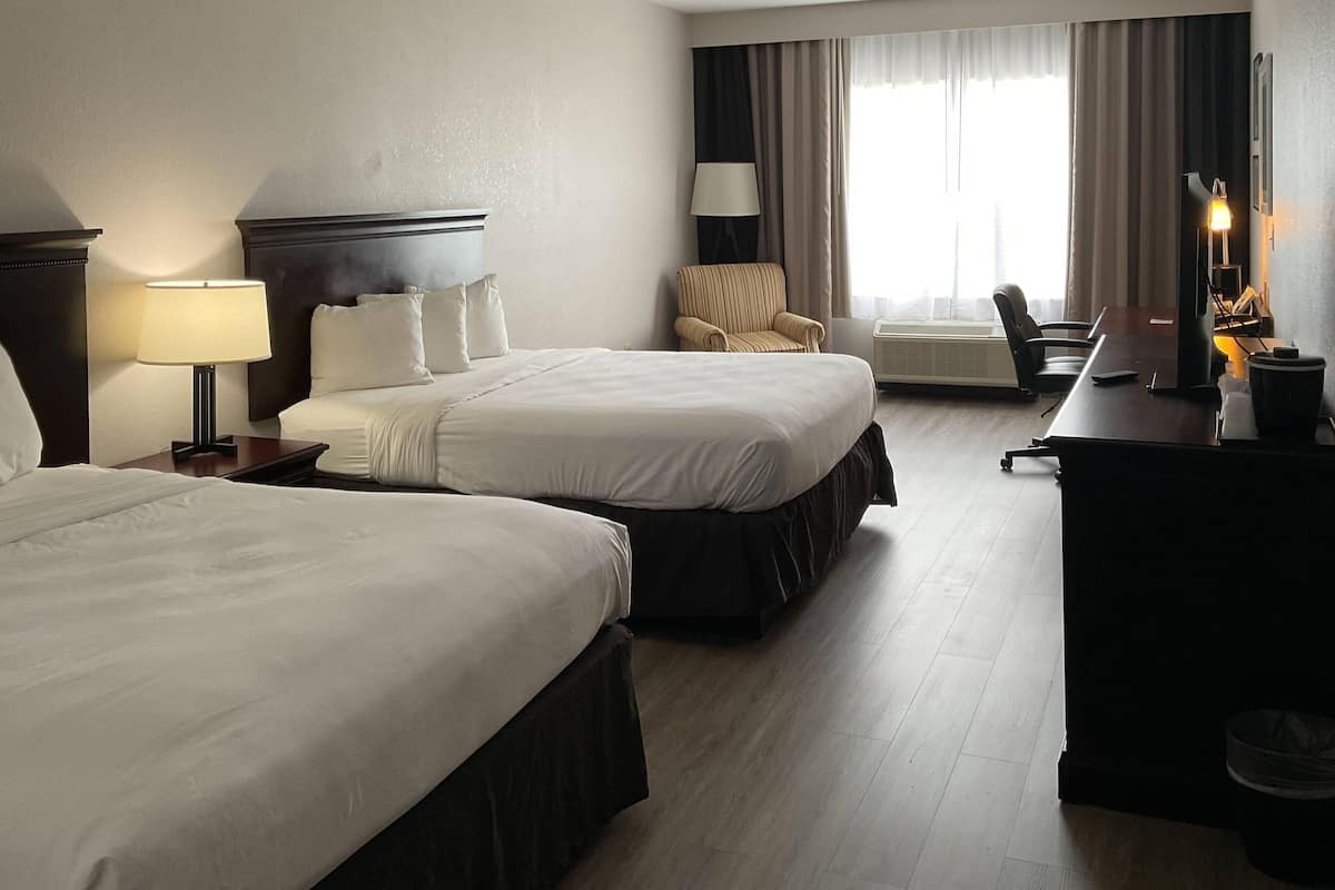 A hotel room with two beds, a desk, a chair, and a large window with curtains.