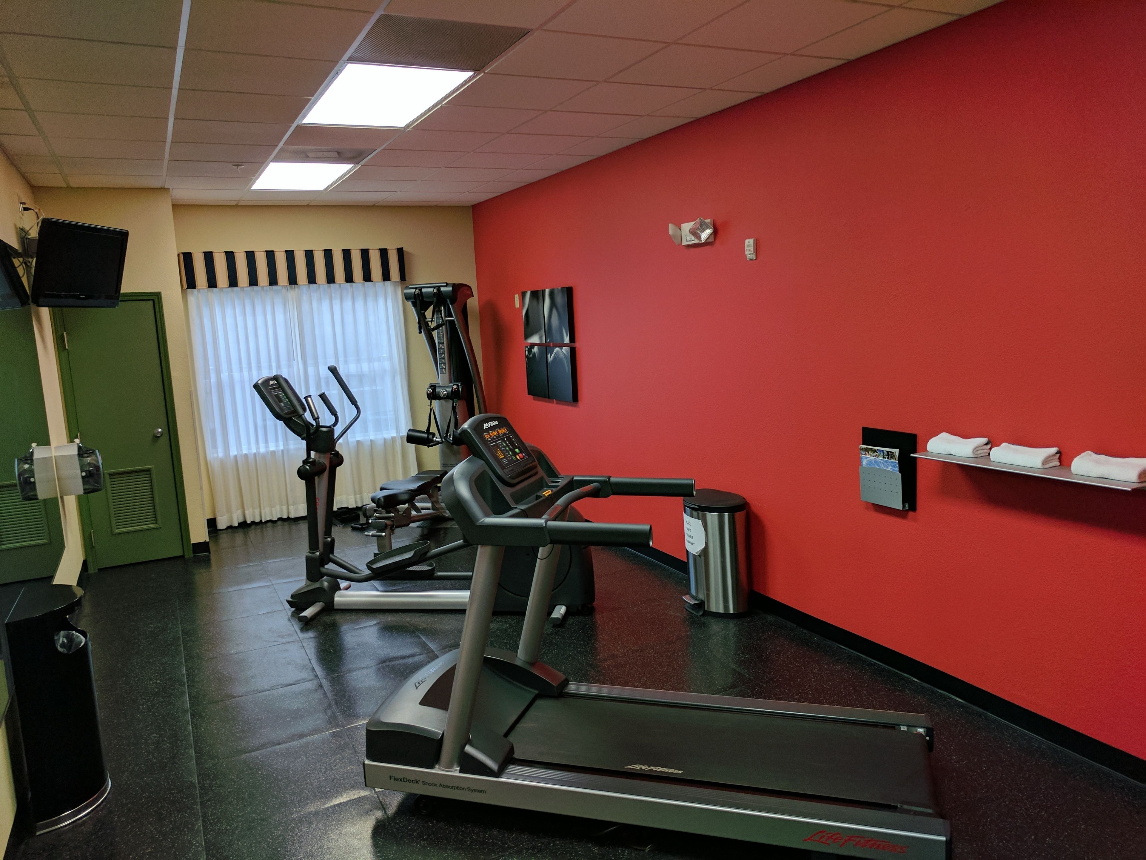Un gimnasio con una pared roja, una cinta de correr y equipo de ejercicio.