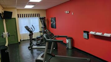 Un gimnasio con una pared roja, una cinta de correr y equipo de ejercicio.