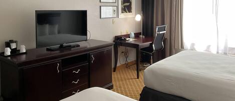 Une chambre d’hôtel avec un lit, un bureau et une chaise, une télévision et des tableaux encadrés au mur.