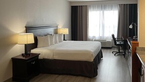 A hotel room with a large bed, two bedside lamps, a desk with a chair, and a large window with curtains. - Country Inn & Suites by Radisson, Tallahassee-University Area, FL (Tallahassee)