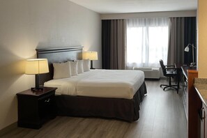 Habitación de hotel con una cama grande, dos lámparas de noche, un escritorio con una silla y un ventanal con cortinas.