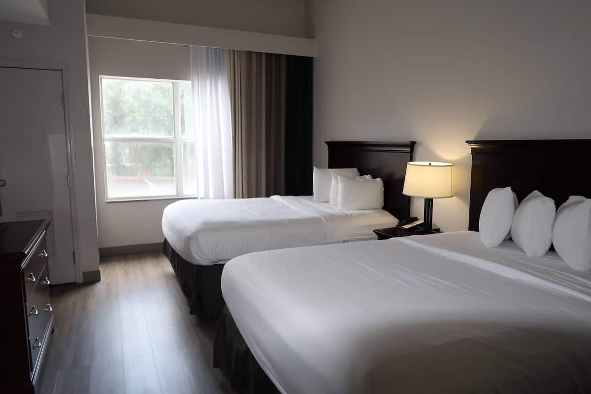 A hotel room with two beds, a dresser, a lamp, and a window with curtains.