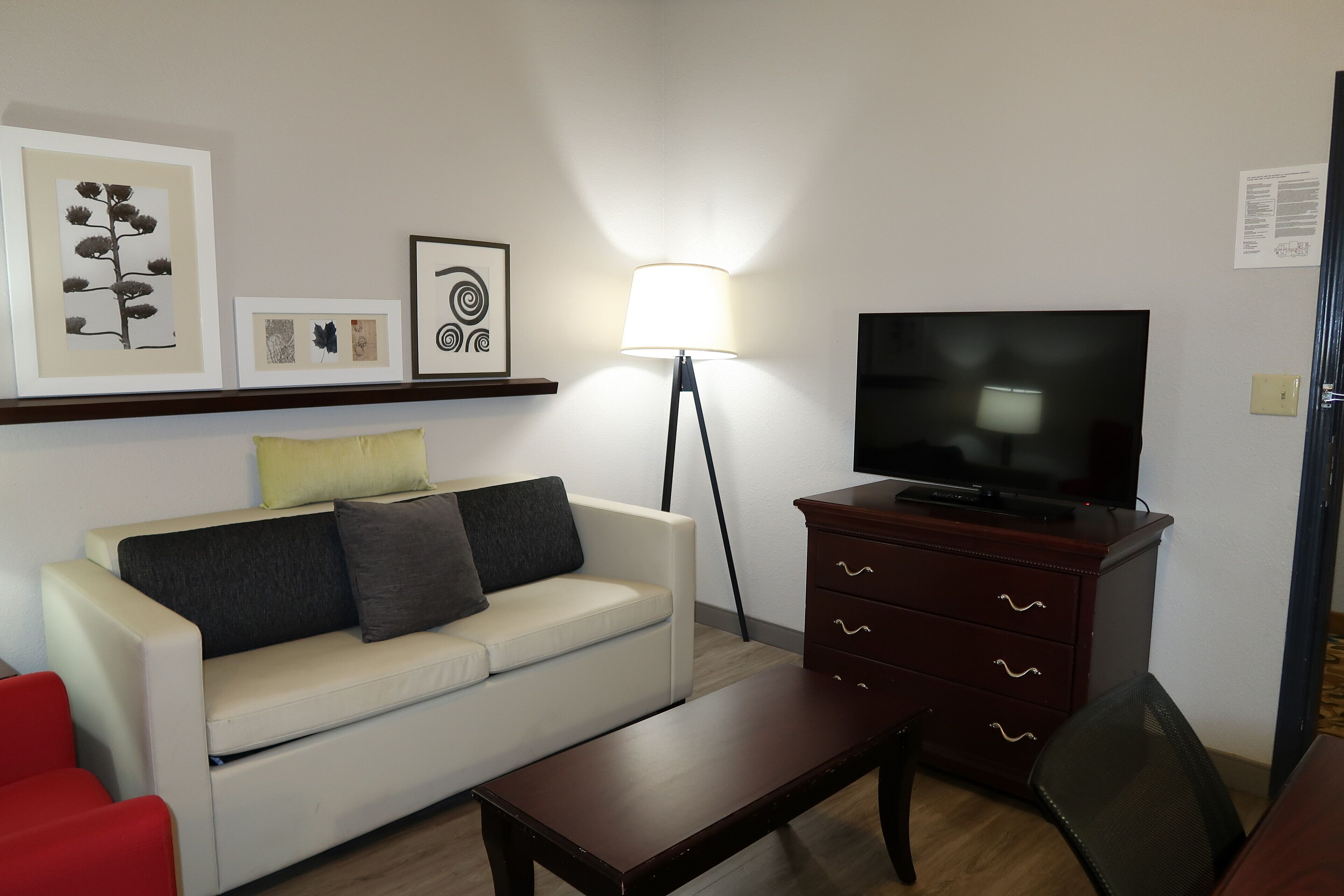 A living room with a sofa, a coffee table, a TV on a wooden cabinet, a floor lamp, and artwork on the wall.