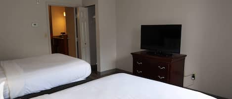 Two single beds with white linens, a television on a wooden dresser, and a door leading to a bathroom.