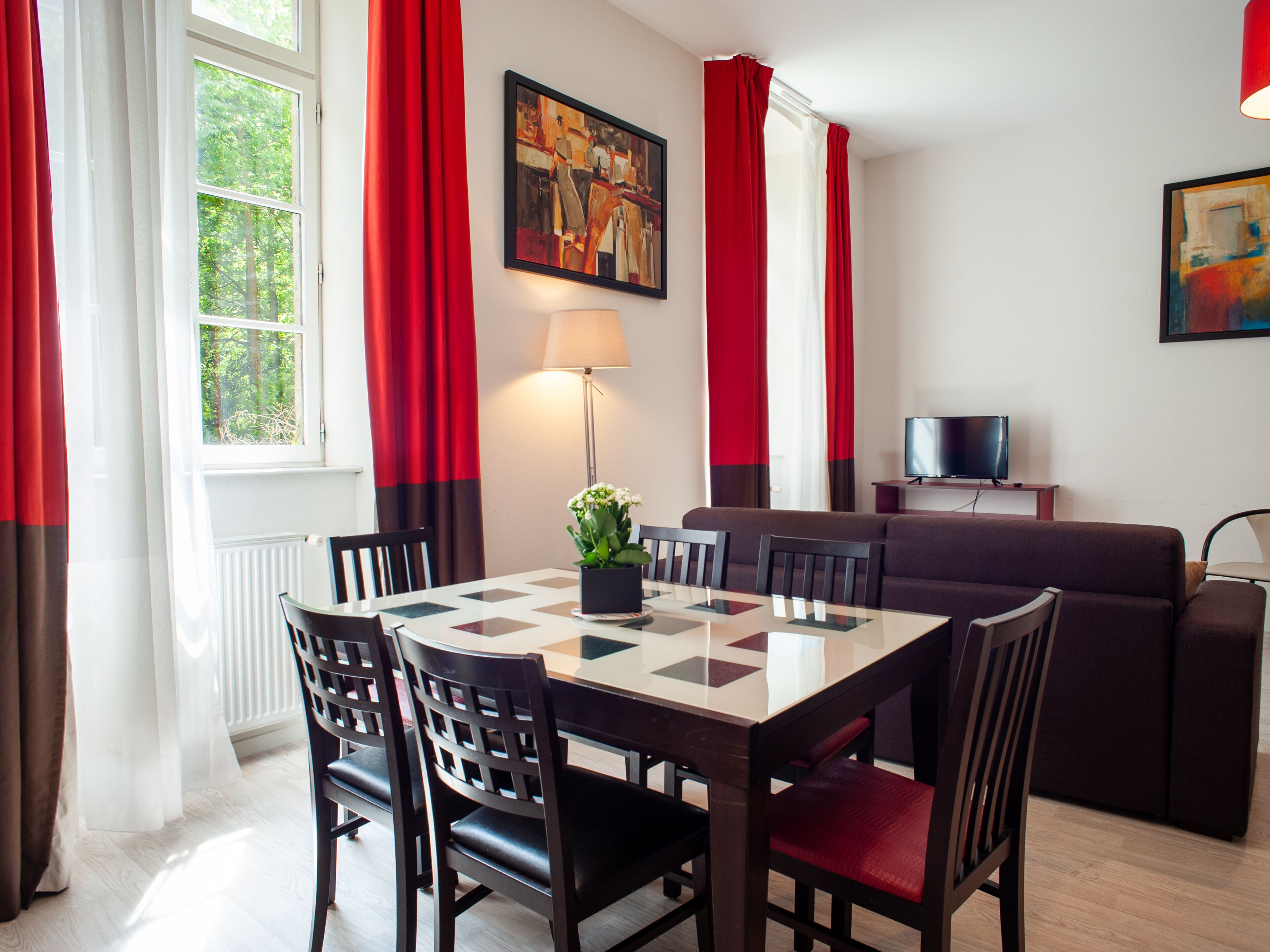 A dining area with a table and chairs, a sofa, a TV, and a painting on the wall.