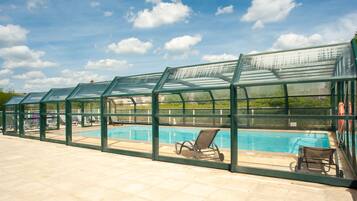 A covered swimming pool with lounge chairs and a glass enclosure.