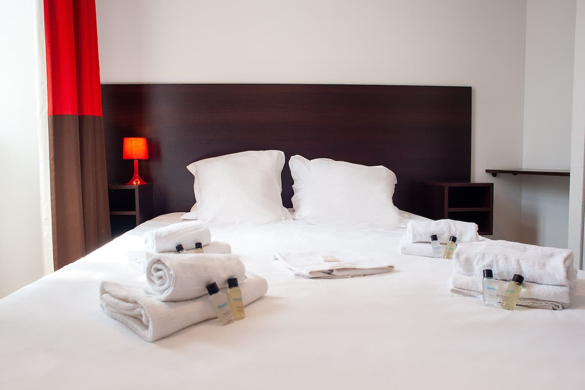 Een net opgemaakt bed met witte lakens en handdoeken, een rode lamp en een donker houten hoofdbord.
