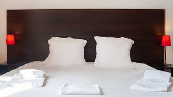 A neatly made bed with white linens and pillows, two bedside lamps with red shades, and a dark wooden headboard.
