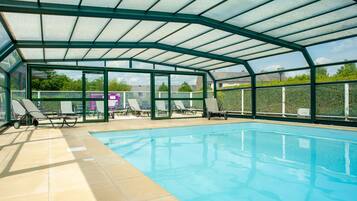 Una piscina interior amb una estructura de vidre, gandules i una vista despejada de l'entorn.