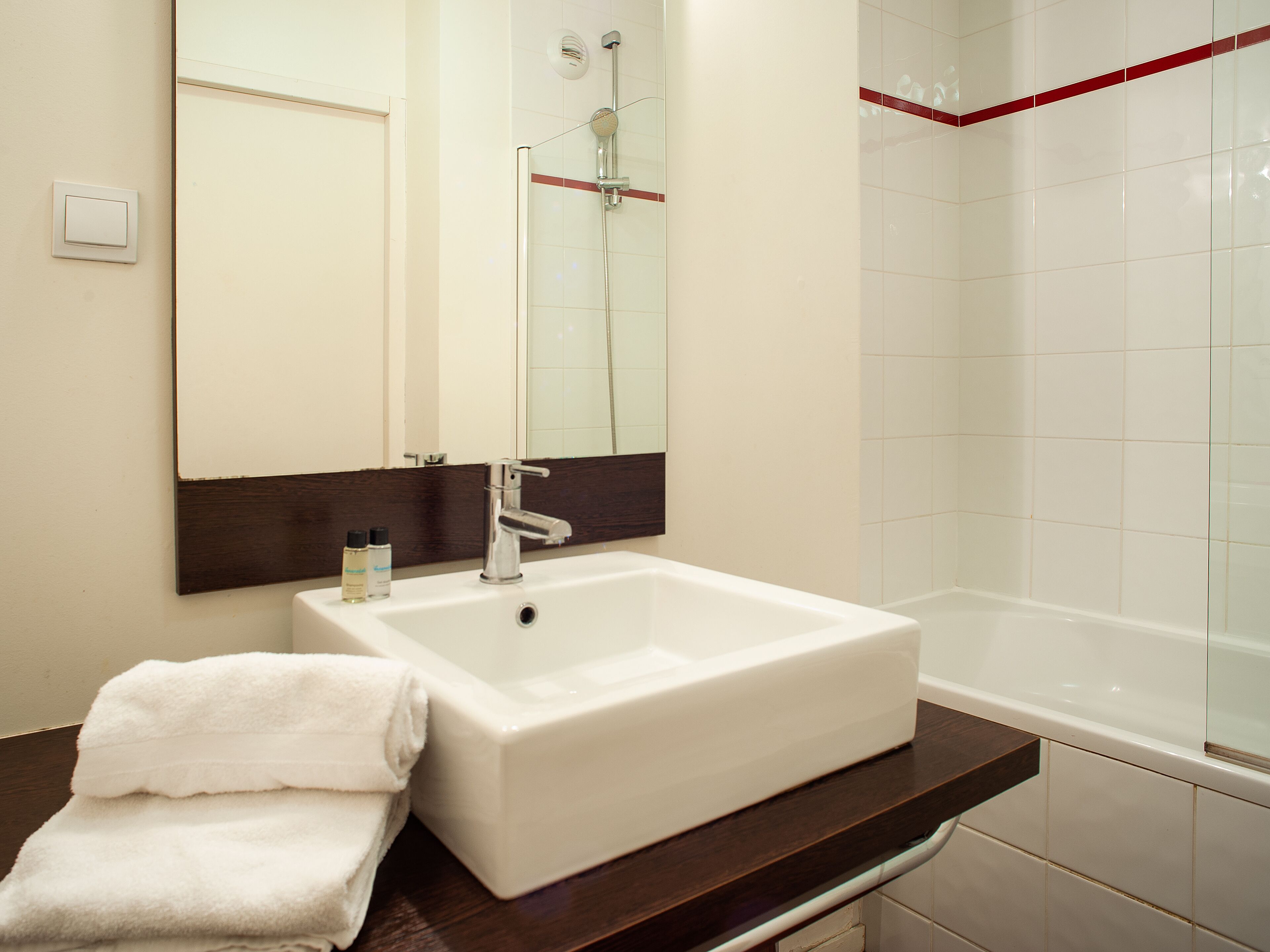 A bathroom with a white sink, a mirror, a shower, and a towel on the counter.