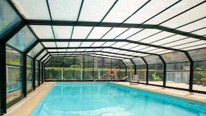 Ein überdachter Pool mit klarem Wasser, umgeben von Glaswänden und einem Dach, mit einem Rettungsring an der Wand.