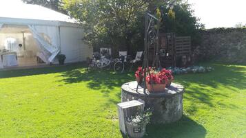 Un jardín bien cuidado con un macizo de piedra circular, una bicicleta y una tienda de campaña blanca al fondo.