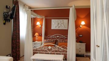 A four-poster canopy bed with a white metal frame, two bedside lamps, a wall-mounted TV, and a decorative wall piece.