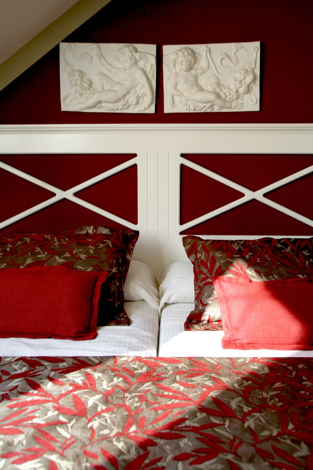Un dormitorio con una decoración en rojo y blanco, que incluye una cama con ropa de cama estampada y dos almohadas rojas.