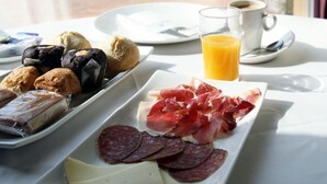 A breakfast table with pastries, cured meats, cheese, and a glass of orange juice.