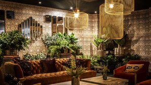 A cozy living room with a brown sofa, a red armchair, and a coffee table. There are multiple plants and a large mirror on the wall. - Waterfront Southport Hotel (Southport)