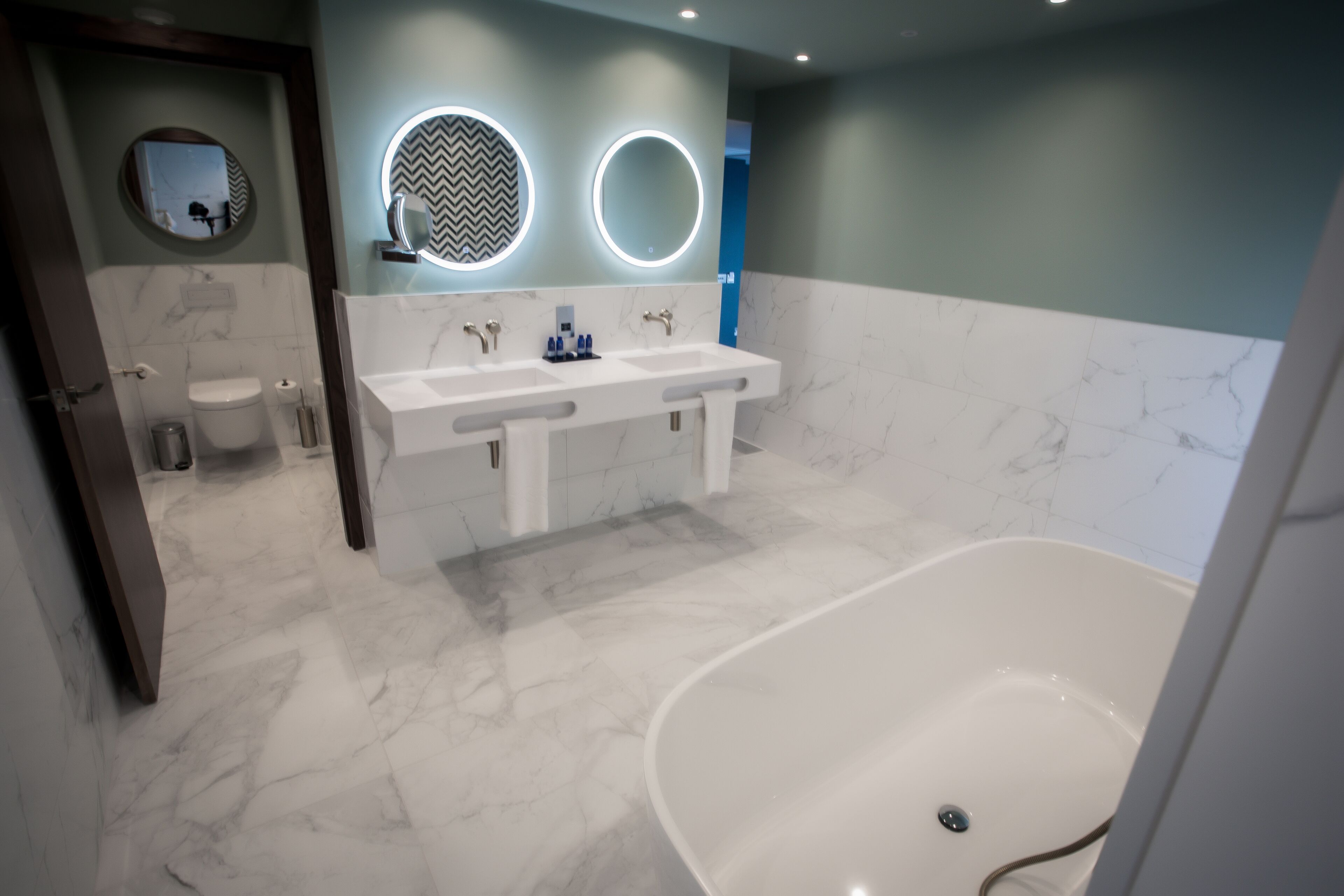 A modern bathroom with a double sink vanity, a freestanding bathtub, and two illuminated mirrors.