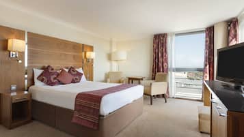A hotel room with a large bed, a desk, a TV, and a view of the city.