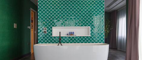 A modern bathroom with a freestanding bathtub, a shelf with toiletries, and a green tiled wall.