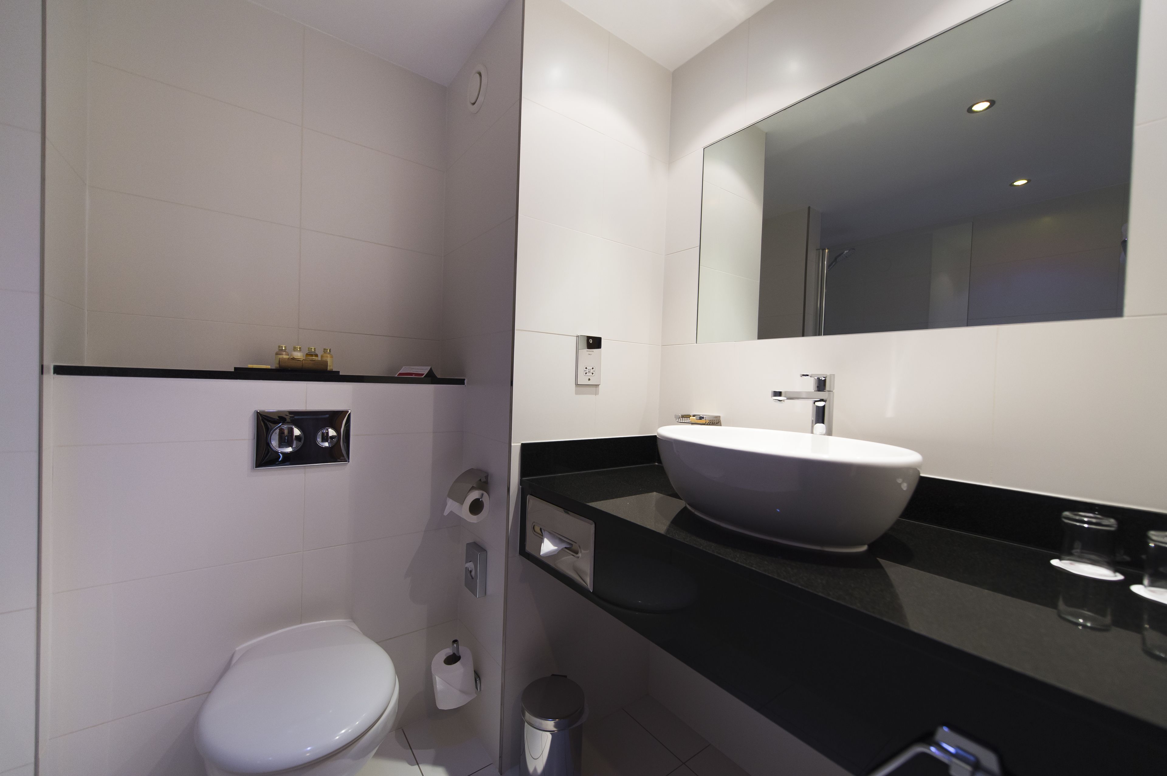 A modern bathroom with a white toilet, a black countertop, a white sink, and a mirror above the sink.