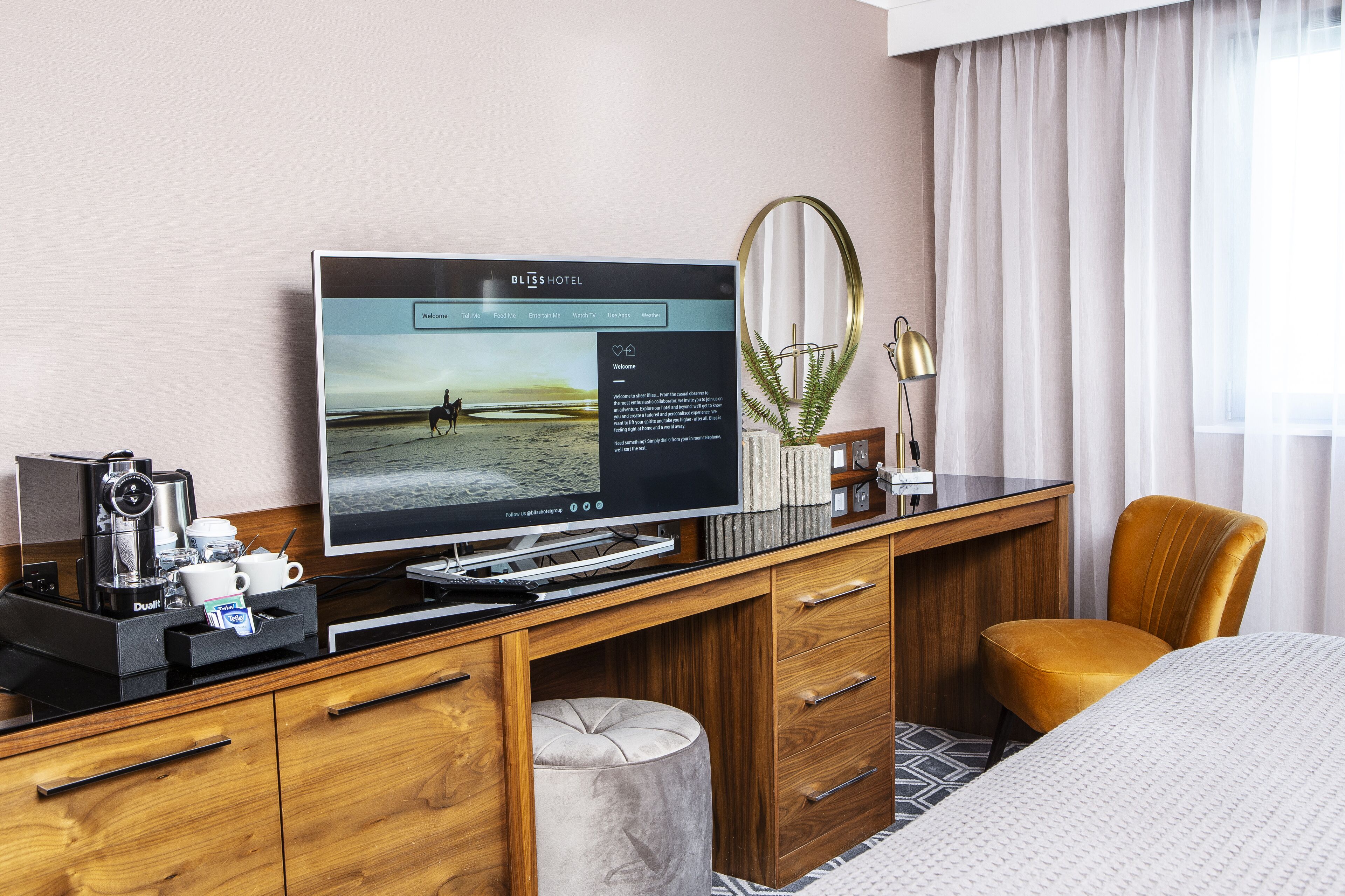 Hotellihuone, jossa on puinen työpöytä, taulutelevisio, kahvinkeitin ja mukava sänky.