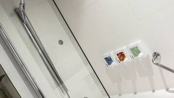 Un baño moderno con ducha envuelta en vidrio, una bañera y tres dispensadores de jabón de colores en la pared.