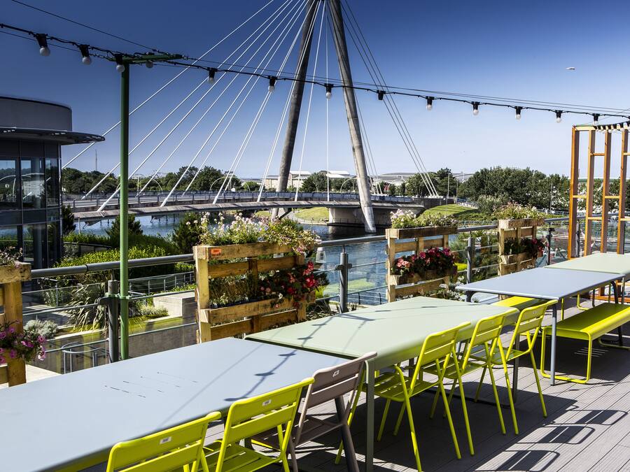Un espacio al aire libre con mesas y sillas, con vista a un río y un puente.