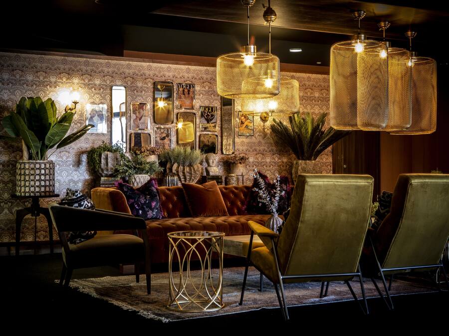 Ein gemütlicher Loungebereich mit einer bequemen Couch, einem runden Couchtisch und zwei Sesseln. Dekorative Wandspiegel und eine gemusterte Tapete sind vorhanden.