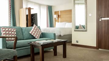 A hotel room with a sofa, a chair, a small table, a bed, a mirror, and a door.